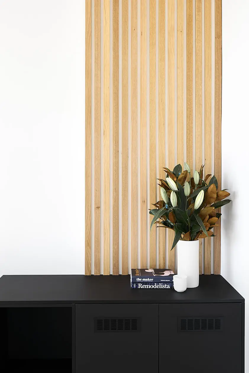 Modern interior design in Hobart featuring a striking wooden slat wall and chic black storage unit, elegantly styled with a fresh floral arrangement.