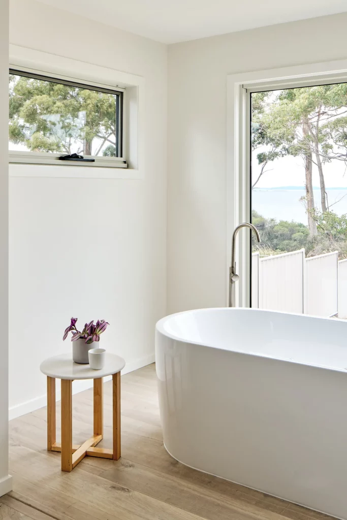 Minimalist and serene bathroom design by an interior designer in Hobart, featuring a freestanding tub with scenic views and subtle decor accents.